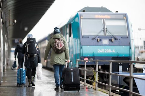  Reisende gehen im Bahnhof Westerland über den Bahnsteig zu einem wartenden Zug