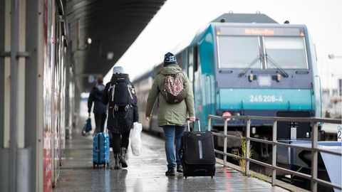  Reisende gehen im Bahnhof Westerland über den Bahnsteig zu einem wartenden Zug