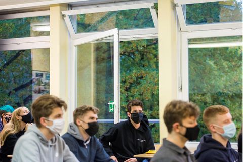Schüler einer Schulklasse sitzen vor einem offenen Fenster