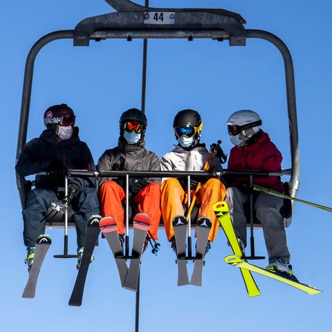 Skifahrer mit Gesichtsmasken fahren im Sessellift des Skigebiets Verbier in den Schweizer Alpen. 