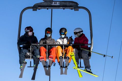 Skifahrer mit Gesichtsmasken fahren im Sessellift des Skigebiets Verbier in den Schweizer Alpen. 