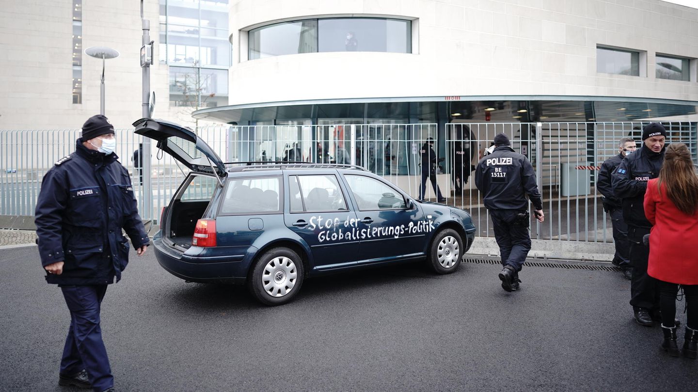 Ein Auto steht vor dem Tor des Bundeskanzleramts. Auf der Tür ist die Aufschrift: "Stop der Globailierungs-Politik" zu lesen