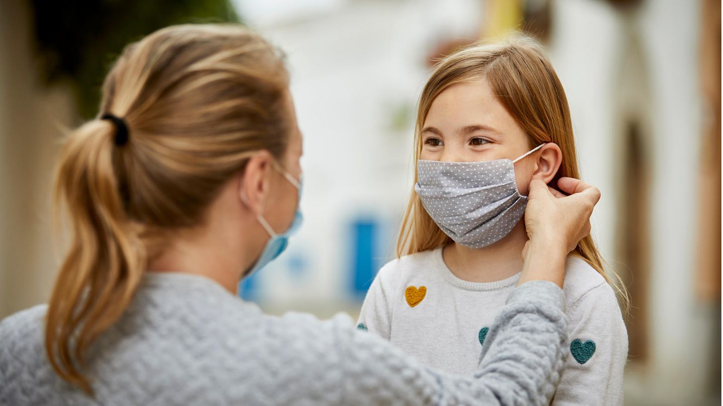 Kinder und Corona: Eine Frau setzt einem Kind einen Mund-Nasen-Schutz auf