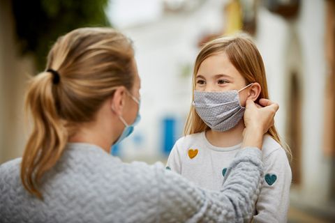 Kinder und Corona: Eine Frau setzt einem Kind einen Mund-Nasen-Schutz auf