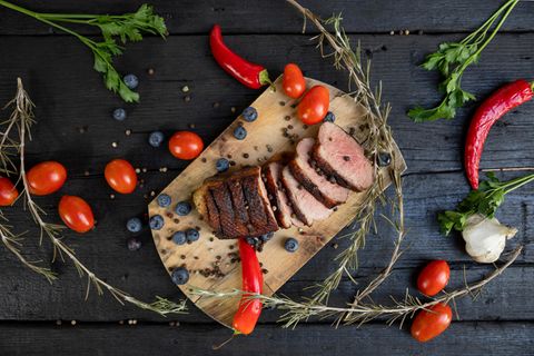 Weihnachtsbraten mit Heidelbeeren, Tomaten, Paprika und Rosmarin auf einem Holzbrett serviert