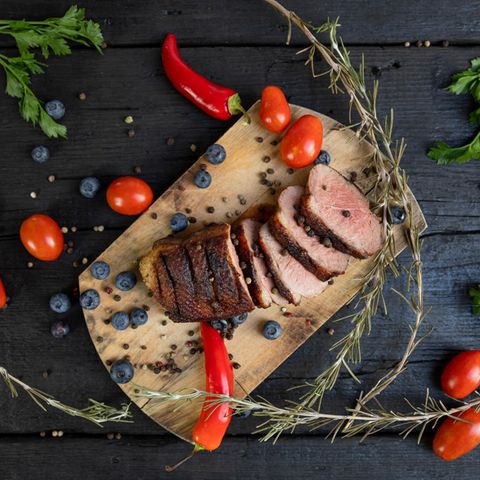 Weihnachtsbraten mit Heidelbeeren, Tomaten, Paprika und Rosmarin auf einem Holzbrett serviert