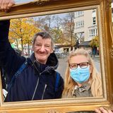 Micha und Ines Sydow posieren mit Bilderrahmen am Franz-Naumann-Platz. Gleich nebenan, in der Residenzstraße 109 befindet sich die Eventgaststätte „Kastanienwäldchen“ von Norbert Raeder. Der sozial engagierte Gastronom nimmt dort werktags ab 16 Uhr Kleiderspenden für Bedürftige entgegen