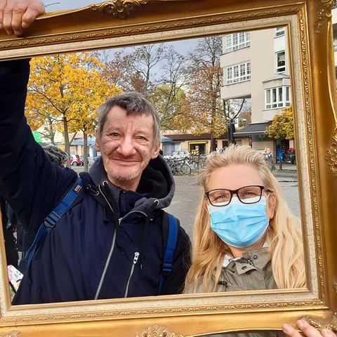 Micha und Ines Sydow posieren mit Bilderrahmen am Franz-Naumann-Platz. Gleich nebenan, in der Residenzstraße 109 befindet sich die Eventgaststätte „Kastanienwäldchen“ von Norbert Raeder. Der sozial engagierte Gastronom nimmt dort werktags ab 16 Uhr Kleiderspenden für Bedürftige entgegen