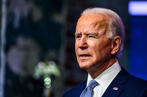 Joe Biden - ein älterer Mann mit weißen, zurückgekämmten Haaren – steht im blauen Anzug vor einem verschwommenen Hintergrund