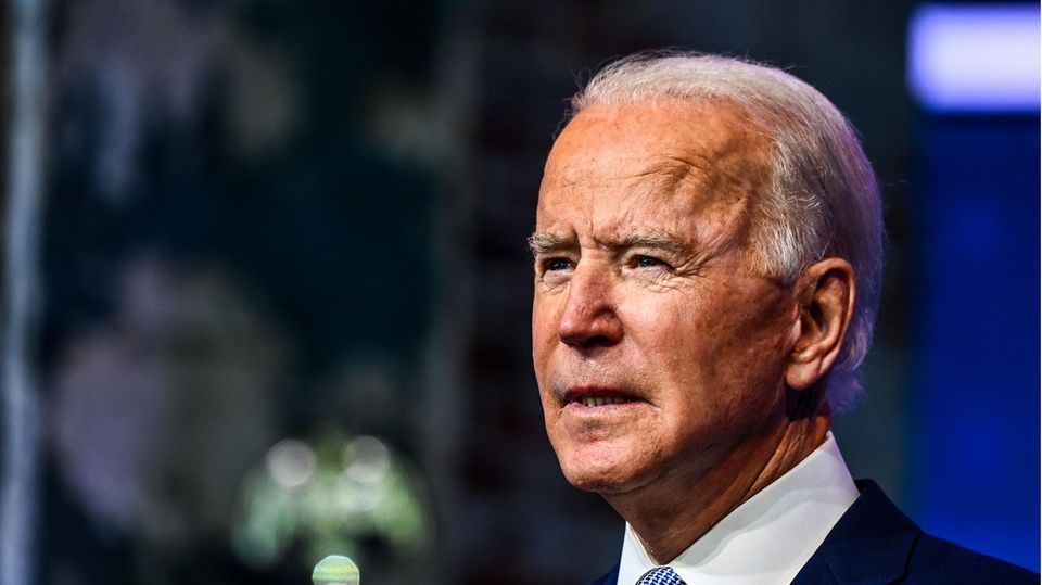 Joe Biden - ein älterer Mann mit weißen, zurückgekämmten Haaren – steht im blauen Anzug vor einem verschwommenen Hintergrund