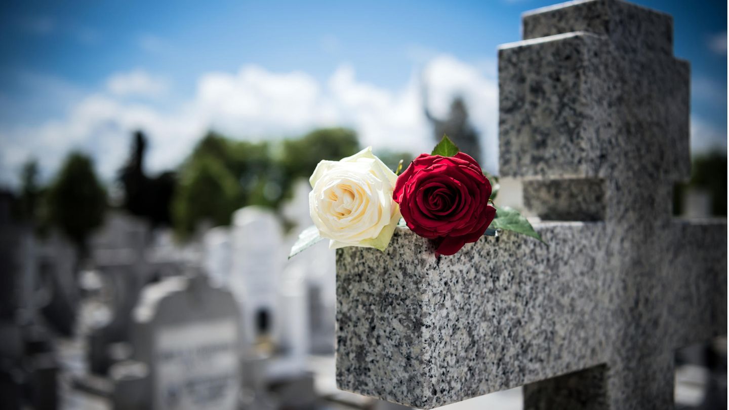 Friedhofskreuz mit einer weißen und einer roten Rose darauf
