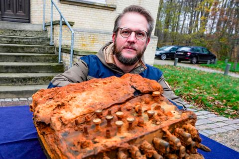 Ein Mann mit Brille und graublondem Seitenscheitel schaut über einen rostigen Klumpen, der an eine Schreibmaschine erinnert.
