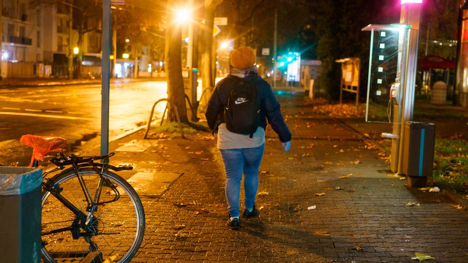 Eine Frau mit einem Rucksack geht in der Dunkelheit durch eine beleuchtete Straße