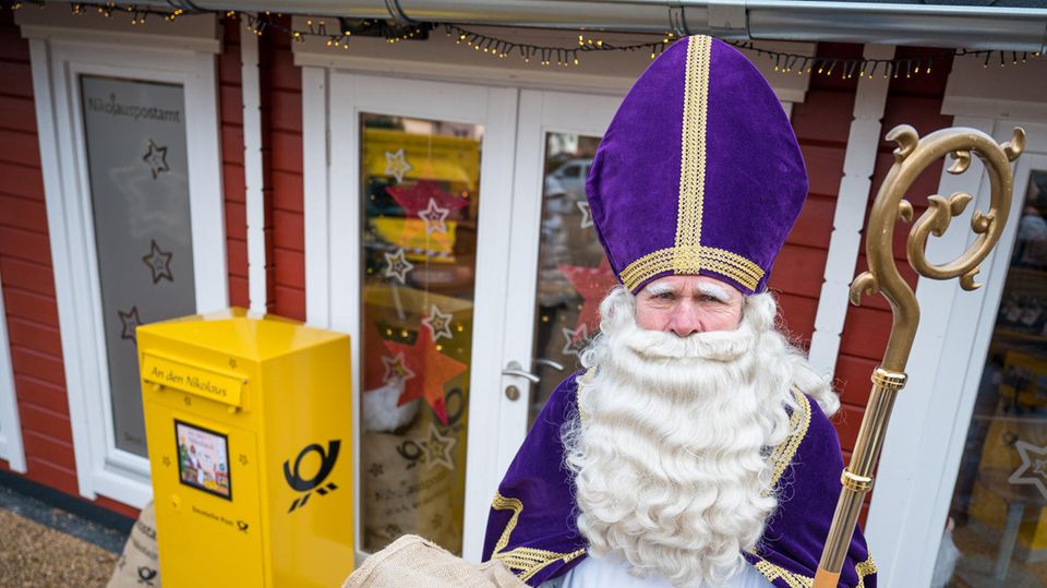 Nikolaus Postamt Saarland Ein Mann mit weißem Vollbart, violettem Bischofstab steht vor einem gelben Briefkasten