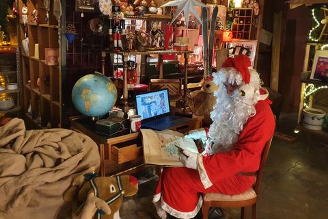 Ein Mann in einem Weihnachtsmann-Kostüm sitzt mit Smartphone und Tablet an einem kleinen Schreibtisch