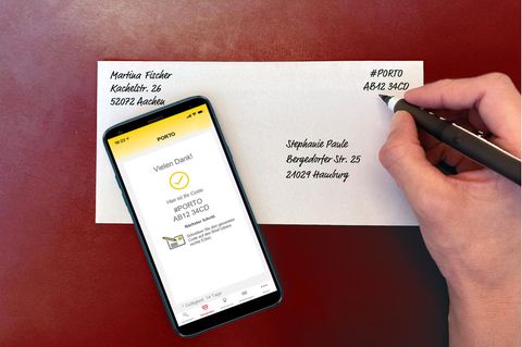 Eine Hand, die einen in der "Post & DHL"-App generierten Porto-Code auf einen Briefumschlag schreibt