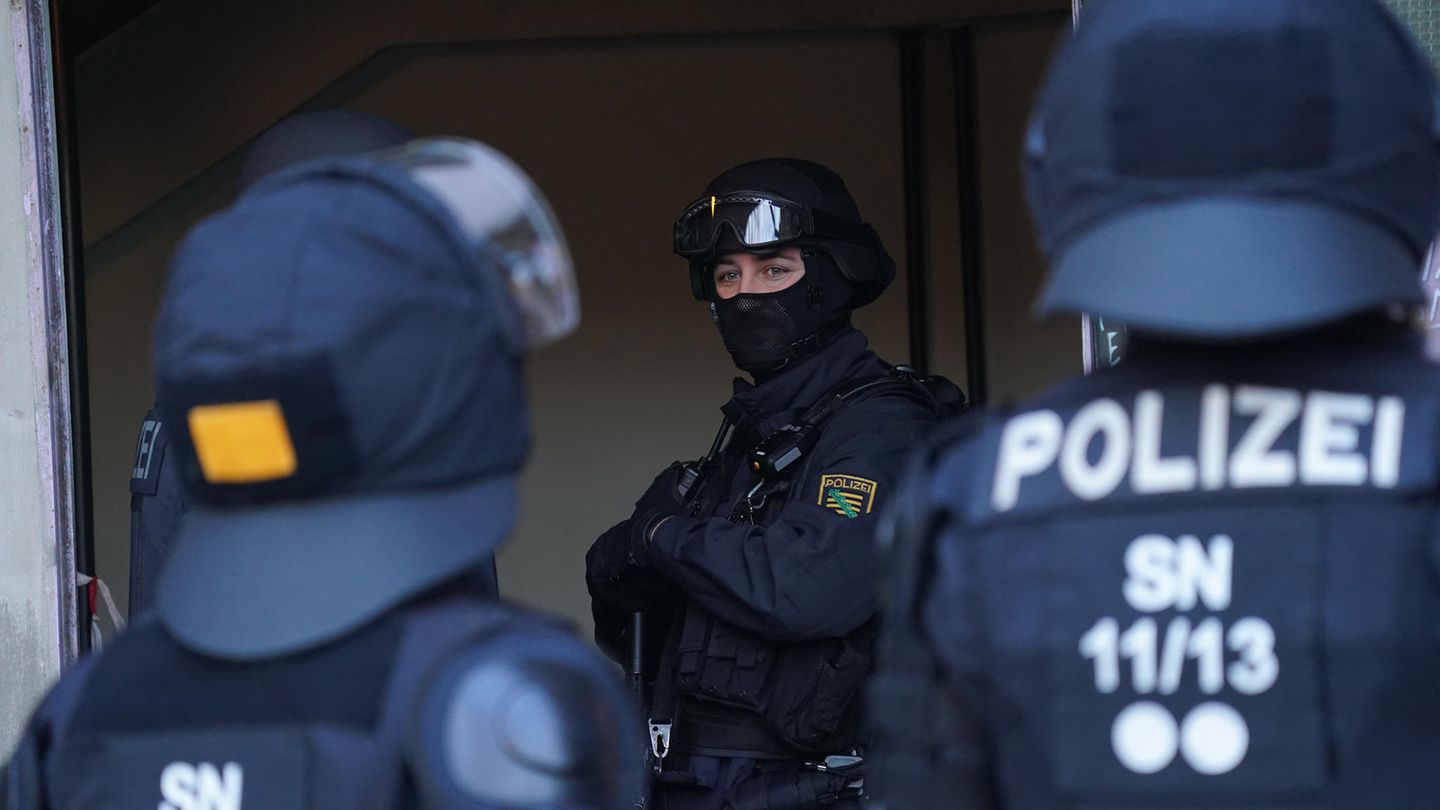 Drei schwer bewaffnete Polizisten in Schutzkleidung stehen im Eingangsbereich eines Gebäudes