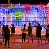 Cali: Weihnachtsfiguren mit Masken  Bewohner der Stadt Cali in Kolumbien betrachten die durch die Straßen rollenden Weihnachts-Trucks. Die Personen auf den Wagen und die Illumination berücksichtigen die Pandemie – Mund-Nasen-Schutz inklusive.