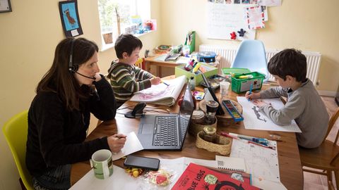 Eine Mutter arbeitet zuhause, während ihre beiden Kinder neben ihr für die Schule lernen