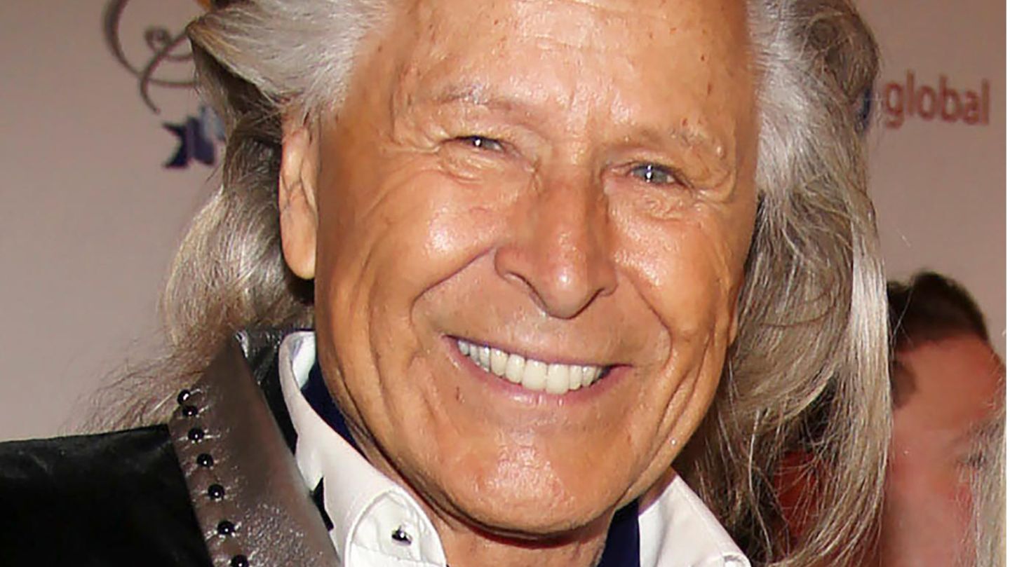 Ein Mann mit weiß-grauer, zurückgekämmter Mähne lächelt mit gebleckten Zähnen in die Kamera