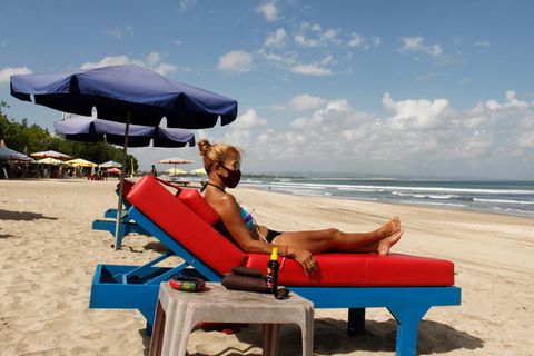 Eine Touristin auf Bali trägt beim Sonnen am Strand den obligatorischen Mund-Nasenschutz