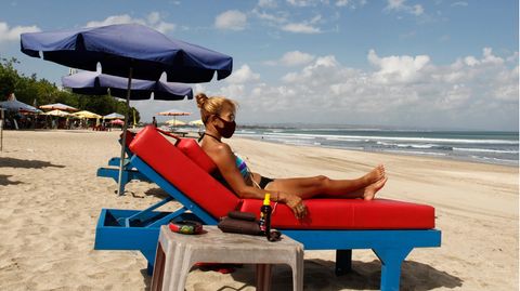 Eine Touristin auf Bali trägt beim Sonnen am Strand den obligatorischen Mund-Nasenschutz