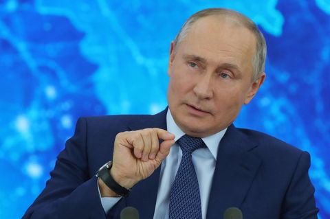 Vor einer blau beleuchteten Weltkarte sitzt Russlands Präsident Wladimir Putin im Anzug und gestikuliert mit der rechten Hand