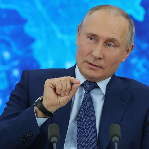 Vor einer blau beleuchteten Weltkarte sitzt Russlands Präsident Wladimir Putin im Anzug und gestikuliert mit der rechten Hand