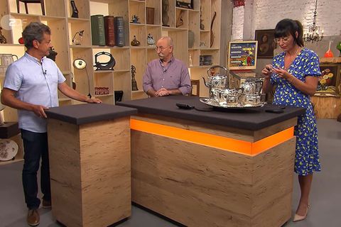 "Bares für Rares"-Expertin Heide Rezepa-Zabel untersucht das Silber von Jean-Jacques Basin (l), während Horst Lichter Smalltalk macht. 
