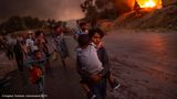 Lesbos, Griechenland: Am 9. September 2020 zerstört im Flüchtlingslager Moria auf der griechischen Insel Lesbos ein Feuer die Unterkünfte von 13.000 Menschen, darunter 4.000 Kinder. Sie sind von Krieg und Gewalt geflohen. Sie haben unter elenden Bedingungen ausgeharrt, viele seit Jahren. Das Lager ist überfüllt, Krankheiten grassieren, immer wieder werden Lebensmittel und sauberes Wasser knapp. Und nun das Feuer. Es breitet sich rasend schnell aus, den Flüchtlingen bleibt nur, in die Hand zu nehmen, was sie greifen können. Unter den vielen Bildern von dieser Inferno-Nacht hat der griechische Fotograf Angelos Tzortzinis die eindrucksvollsten vom Leiden der Kinder gemacht. Und jenes Foto, das alles gleichzeitig zeigt: Flucht und Tapferkeit, Fassungslosigkeit und Hilfsbereitschaft in höchster Not. Die Stärke des Kleinen, der dem noch Kleineren die heile Haut bewahrt. Unter den nach UNO-Schätzungen gegenwärtig rund 79,5 Millionen Menschen auf der Flucht sind etwa 32 Millionen Kinder und Jugendliche.   Angelos Tzortzinis, geboren in Athen, hat an der Leica Academy of Creative Photography studiert und seither überwiegend als freier Fotograf gearbeitet. Er hat aus Georgien berichtet und vom Erdbeben in Haiti 2010, vom "Arabischen Frühling" in Kairo und dem Krieg in Libyen. Vor allem aber beschäftigt ihn die Situation der Flüchtlinge in seinem Heimatland.
