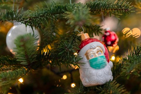 An einem Weihnachtsbaum hängt Weihnachtsschmuck in Form eines Weihnachtsmannes, der eine Maske trägt