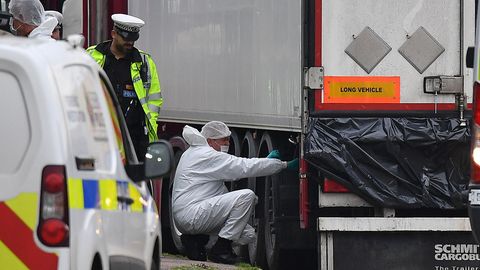 Ein Polizist in neongelber Jacke beobachtet einen Kriminaltechniker in weißem Overall, der neben einem Lkw-Auflieger kneit