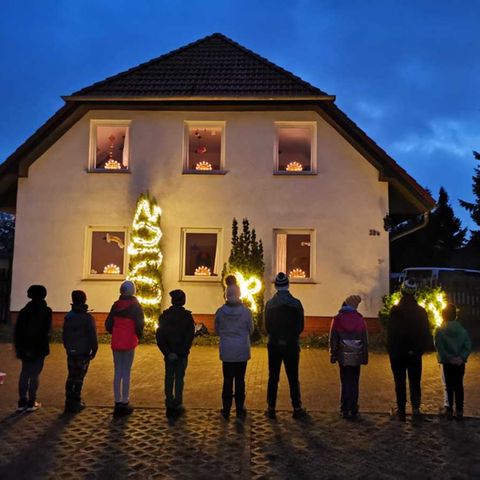 Neun Kinder stehen vor dem beleuchteten Kinderdorfhaus