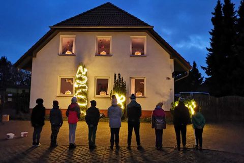 Neun Kinder stehen vor dem beleuchteten Kinderdorfhaus
