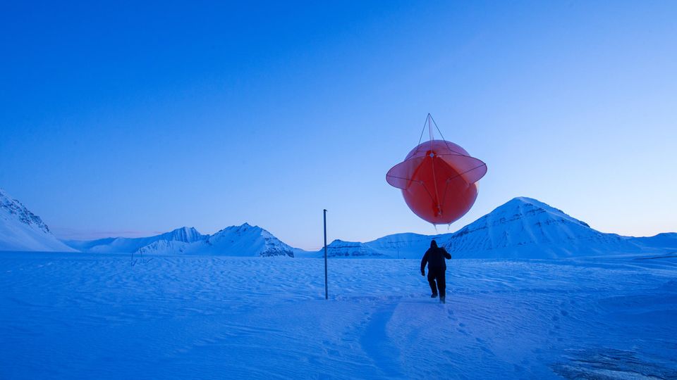 Ein Forscher mit einem Wetterballon in Ny-Ålesund Ein Forscher mit einem Wetterballon in der Eislandschaft von Ny-Ålesund