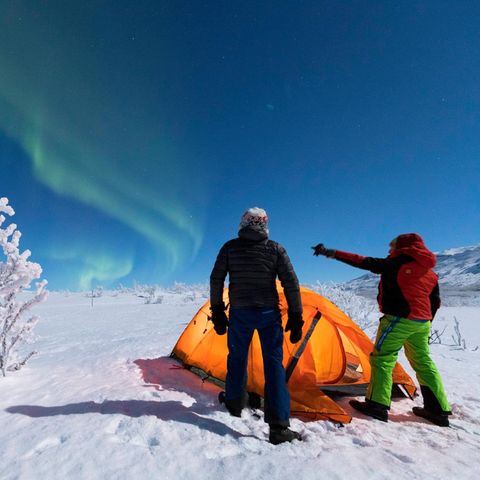 Zwei Camper schauen sich im Schnee in Kiruna das Nordlicht (Aurora Borealis) an