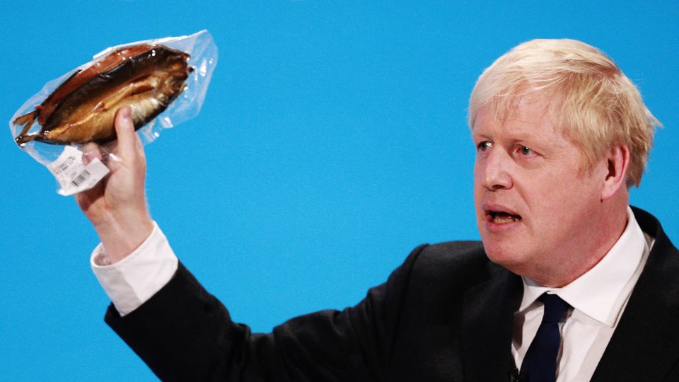 Boris Johnson hält einen eingeschweißten Räucherfisch hoch