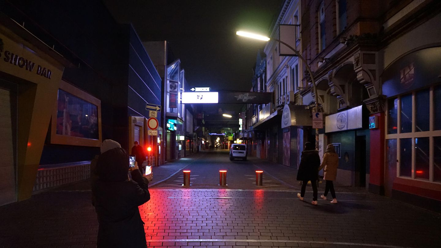 Auf einem Platz fotografiert eine junge Frau mit ihrem Smartphone den Blick in eine überwiegend dunkle Straße hinein