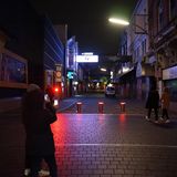 Auf einem Platz fotografiert eine junge Frau mit ihrem Smartphone den Blick in eine überwiegend dunkle Straße hinein