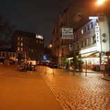 Ein dreieckiger, leerer Kopfsteinpflaster-Platz mit Kneipen und Restaurants am Rand liegt menschenleer da