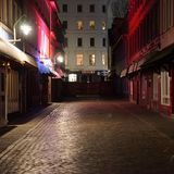 Eine Kopfsteinpflaster-Straße bei Nacht. Links und rechts stehen niedrige Häuser mit großen Fenstern zur Straße.