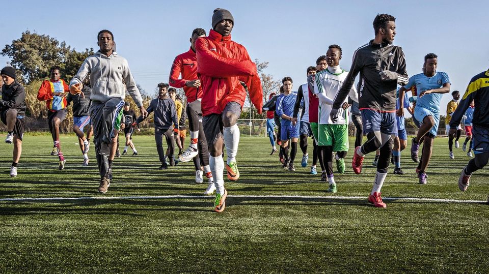 Januar 2020, LESBOS, Moria, GRIECHENLAND, Europa: Paul Asema Yongo, 19, aus Kamerun, will Profifussballer in Europa werden, er ist Co-Trainer und Spieler bei Cosmos FC, beim Fussballtraining mit Gefluechteten aus dem Fluechtlingslager Moria, trainieren ... Links: Vor dem Lockdown hilft Asema (in der
roten Jacke) als Assistenztrainer aus. Viele Flüchtlinge kommen mit zerrissenen Schuhen zum Training