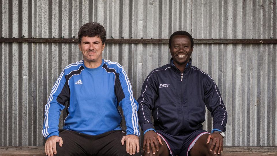 Fußball auf Lesbos (FINAL) >> 11.Dezember 2020, Moria, Lesbos, Griechenland, Europa: Evaggelos Spanos, Alter 55, erfolgreicher Fussball Coach, 1.v.l. und Fluechtling Paul Asema Yongo, 19, 2.v.l. aus Kamerun, will Profifussballspieler in Europa we... Spanos (l.) und Asema auf der Bank. Die beiden sind Freunde geworden