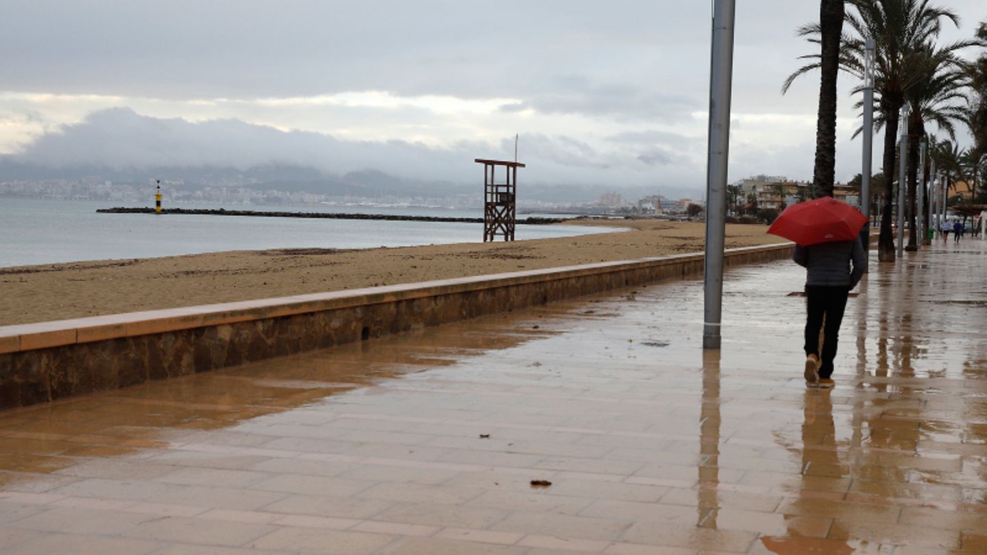 Ein Mann spaziert mit einem Regenschirm am Strand von Palma entlang.