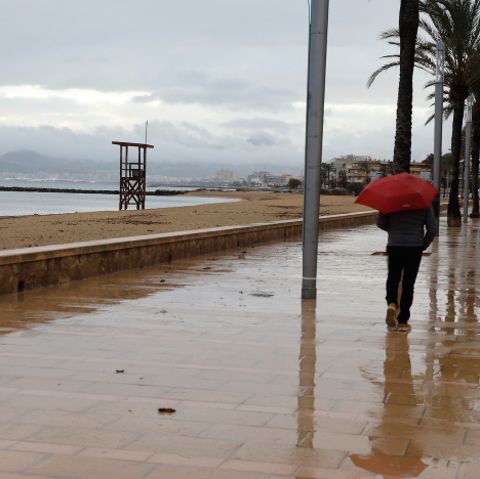Ein Mann spaziert mit einem Regenschirm am Strand von Palma entlang.