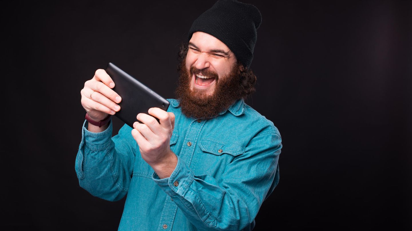 Gaming-Tablet: Ein Mann spielt mit seinem Tablet. Der Mund ist weit aufgerissen, die Augen vor Freude zugekniffen.