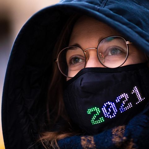 Eine Frau mit Brille trägt eine dunkelblaue Kapuze sowie einen schwarzen Mund-Nasen-Schutz mit bunter "2021"-Stickerei