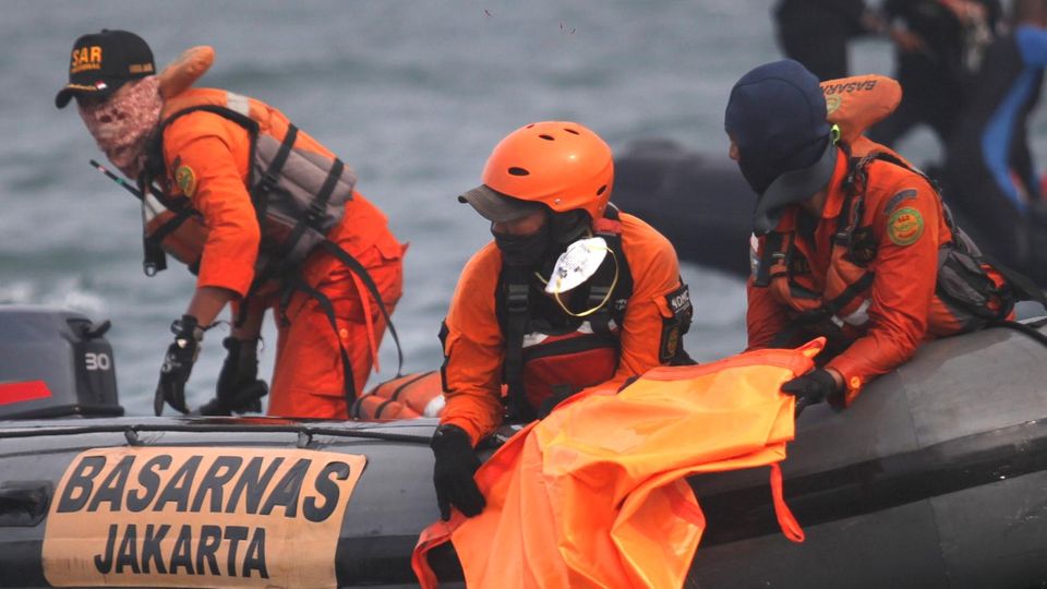 Retter Flugzeugabsturz Indonesien Schlauchboot Meer Von einem dunkelgrauen Schlauchboot aus halten drei Männer in orangen Overalls Ausschau über das Meer