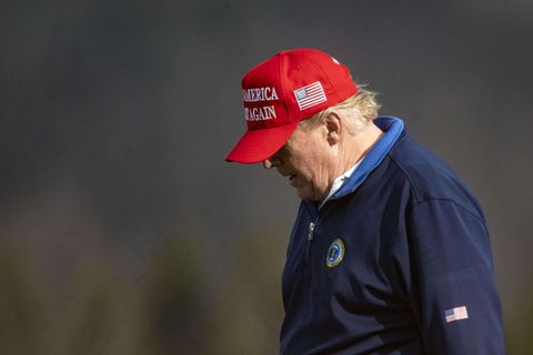 Mit rotem "Make America great again"-Cap und blauem Pullover geht Donald Trump mit gesenktem Kopf über einen Golfplatz