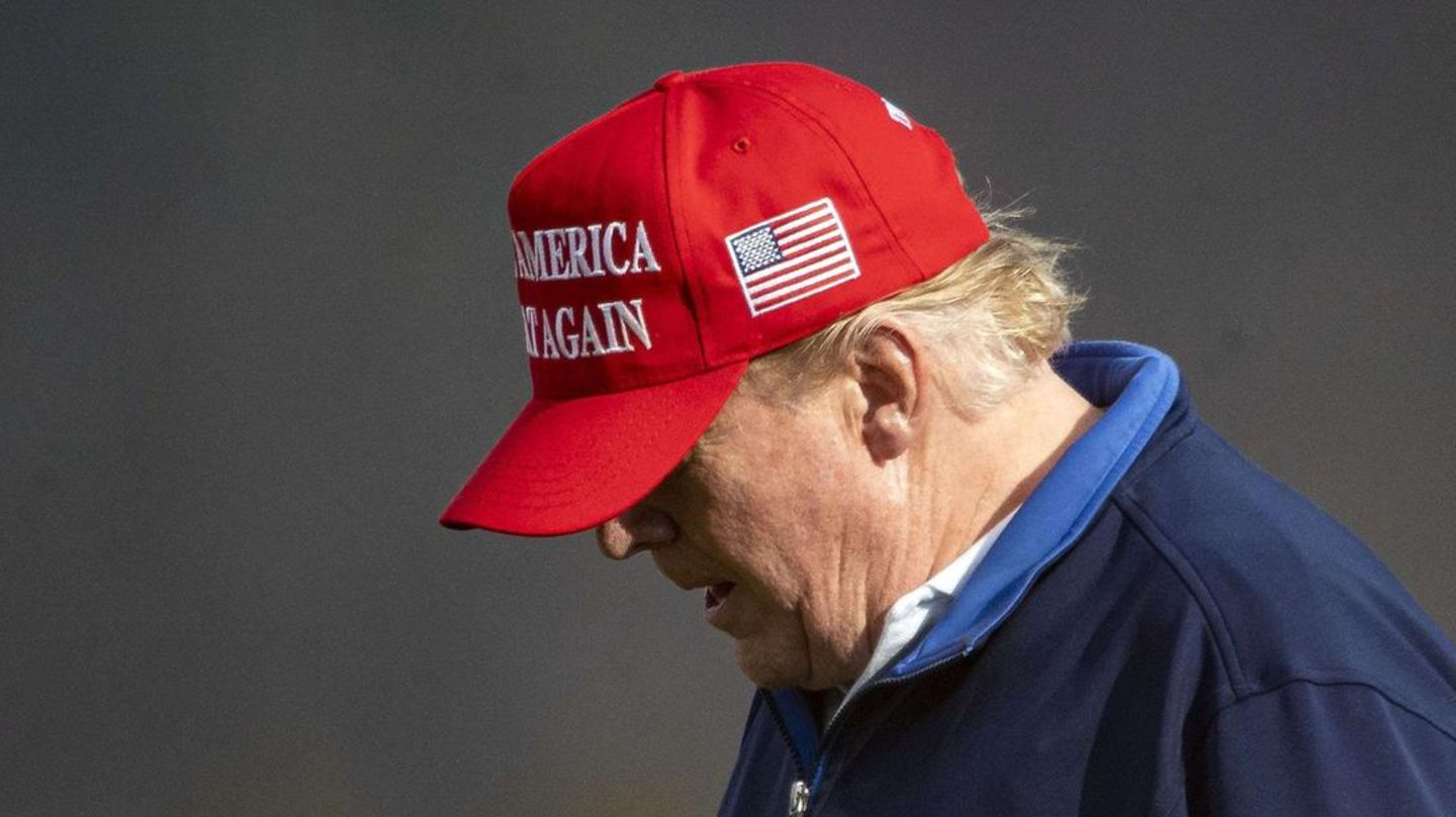 Mit rotem "Make America great again"-Cap und blauem Pullover geht Donald Trump mit gesenktem Kopf über einen Golfplatz